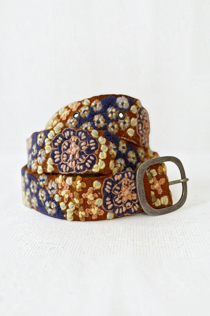 ELSHAM BOUTIQUE wool belt with blue and gold floral embroidery and a rustic metal buckle on a white background