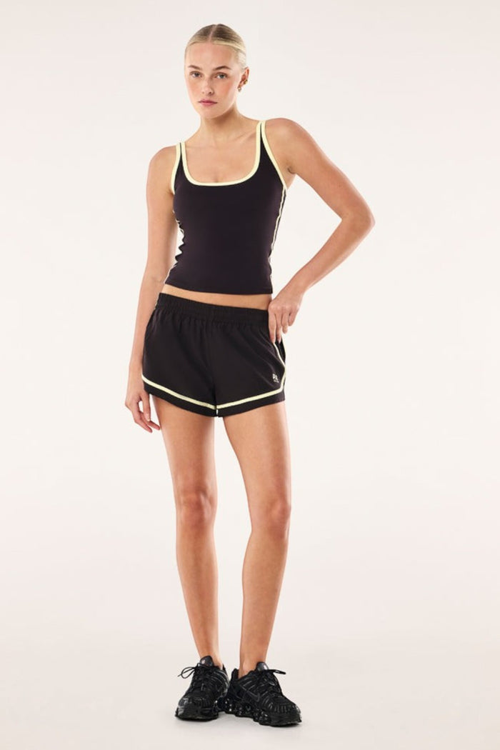 Model wearing ELSHAM BOUTIQUE black athletic shorts with soft yellow trim and matching tank top against a studio backdrop